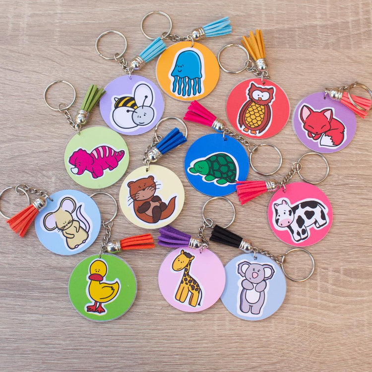 A collection of colorful keychains featuring various cartoon animals, including a jellyfish, bee, owl, fox, dinosaur, otter, turtle, cow, mouse, duck, giraffe, and koala. Each keychain has a matching tassel.