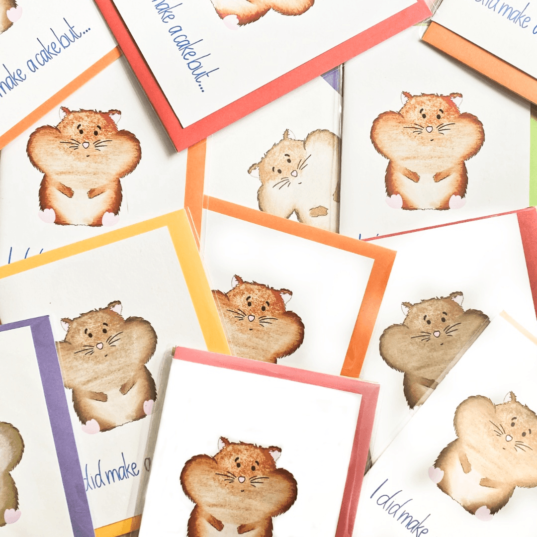 Introducing the Hamster Greeting Card collection, featuring adorable illustrations of hamsters with puffy cheeks holding treats. Each card is bordered in vibrant colors such as orange, red, and purple. The playful text "I did make a cake but..." adds a humorous touch, making these cards perfect for any occasion.