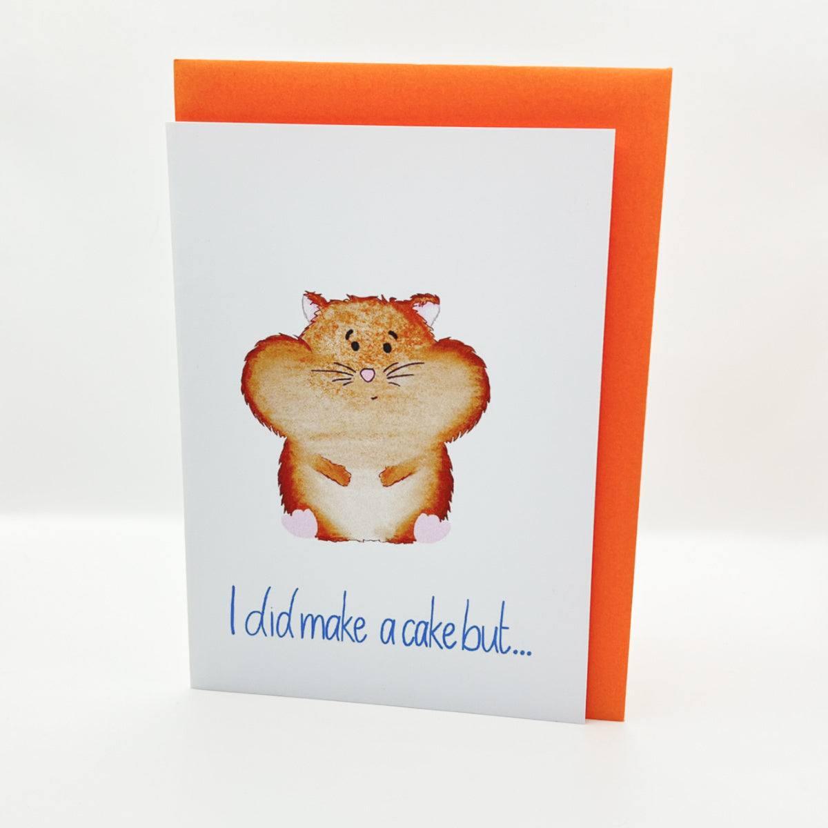 The Hamster Greeting Card features an illustration of a hamster with its cheeks puffed out as if full. The text below the hamster reads, "I did make a cake but..." The card is white and comes with an orange envelope.