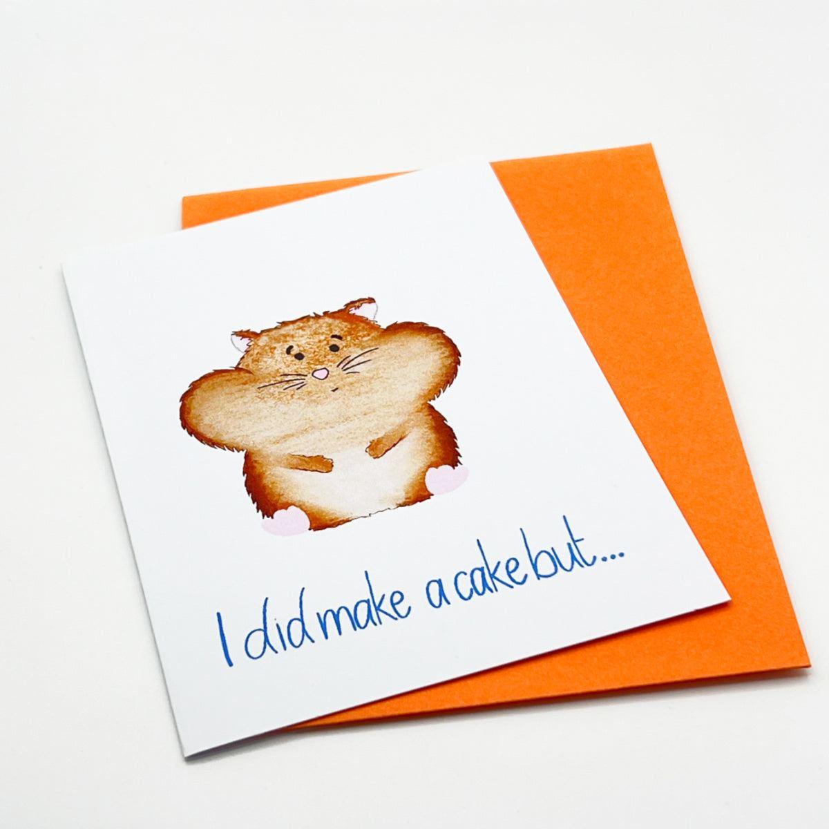 The Hamster Greeting Card showcases a cute, chubby white hamster holding its paws together. The blue handwritten text on the card reads, "I did make a cake but..." An orange envelope is partially visible beneath the card, making it perfect for sending birthday greetings.