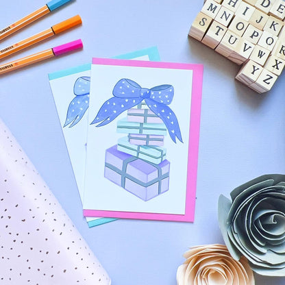 Two Pastel Birthday Cards featuring stacked gifts tied with a bow, surrounded by pens, letter stamps, and decorative paper flowers on a light surface. Celebrate in style with these charming details that make every birthday special.