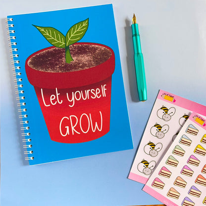 A Let Yourself Grow Notebook with a blue cover featuring a potted plant and the positive quote "Let yourself GROW." Beside it is a teal fountain pen and a sheet of colorful stickers, including mouse faces with bee wings and slices of cake, all on a light blue background.