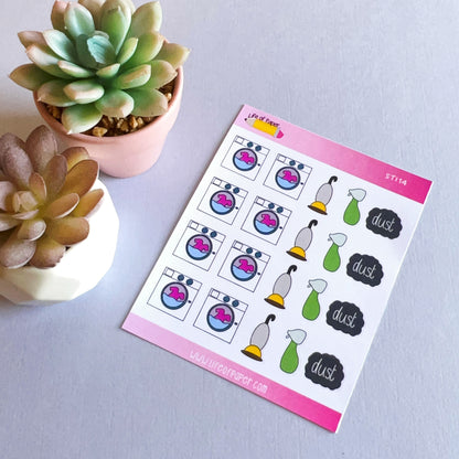 A sheet of colorful Cleaning Planner Stickers is shown next to two small potted succulent plants. The stickers feature illustrations of washing machines, vacuum cleaners, spray bottles, and "dust" text bubbles on a pink-bordered sheet labeled "ST114," perfect for organizing house chores.