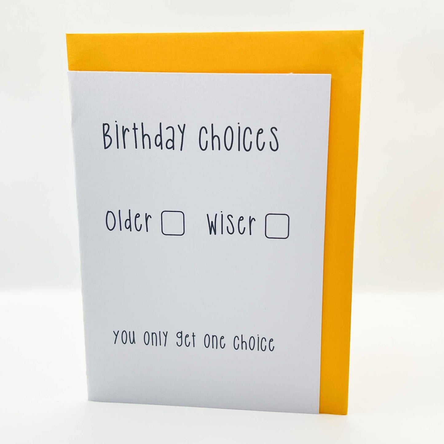 Introducing the Birthday Choices Blank Card, a biodegradable greeting card paired with a yellow envelope. The front of the card features the words "Birthday Choices" followed by two options with checkboxes: "Older" and "Wiser." At the bottom, it humorously states, "You only get one choice." This is the perfect card for an older friend with a great sense of humor.