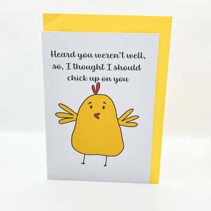 The Chicken up on you Get Well Soon Card features a charming illustration of a yellow chicken and the text "Heard you weren't well, so, I thought I should chick up on you" on the front. The card is presented against a plain white background and includes a bright colored envelope in biodegradable cellophane.