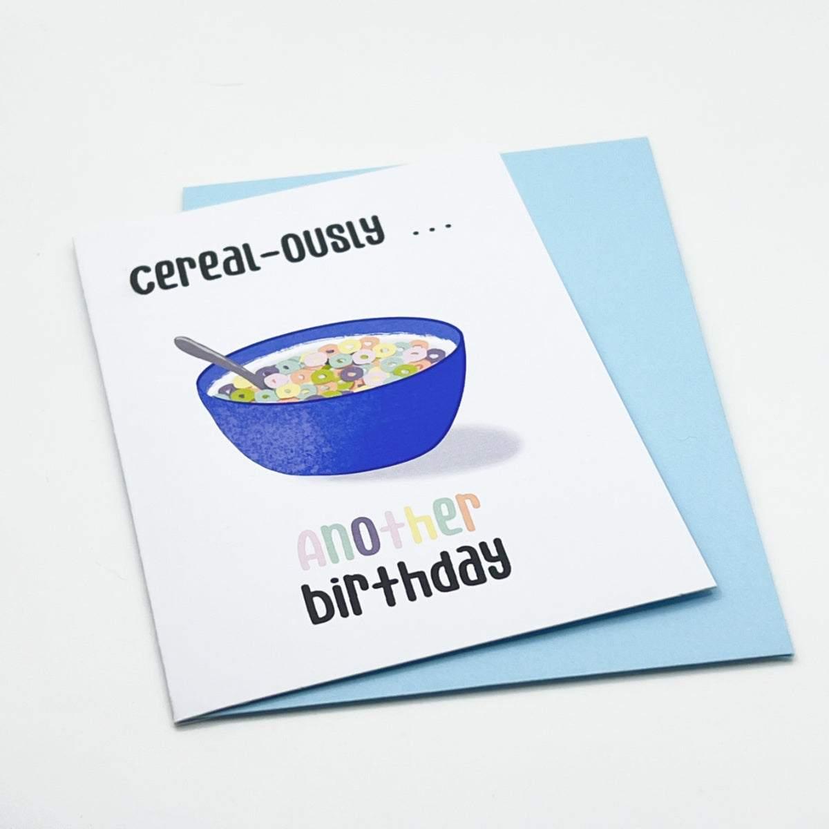 Introducing "Cereal-ously Another Birthday" - a vibrant birthday card featuring an illustration of a blue bowl brimming with colorful cereal and milk, accompanied by a spoon. The playful text above the bowl reads "cereal-ously..." and below it says "another birthday." Ideal for celebrating a friend’s special day, this card comes with a light blue envelope.