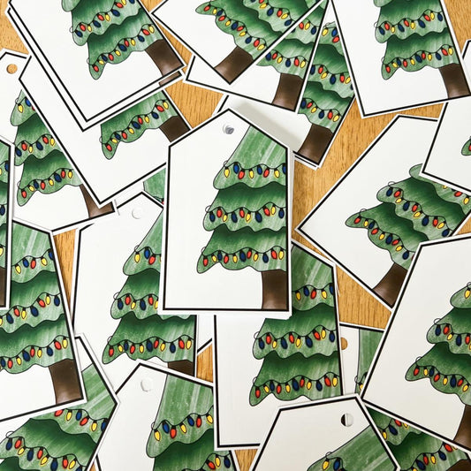 A collection of Christmas Tree Gift Tags, each handmade and showcasing an illustration of a Christmas tree adorned with colorful lights, scattered on a wooden surface.