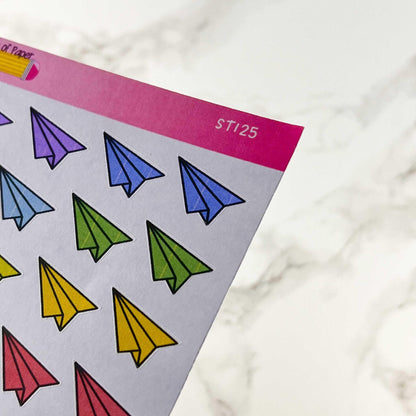 A close-up of a white sheet of Aeroplane Doodle Stickers 2 - Not Quite Perfect Sticker Sheet with a pink header. The stickers, sporting an old branding style, feature paper airplanes in various colors: purple, blue, green, yellow, and red. The sheet background is set against a marble-like surface—now available at a lower price.