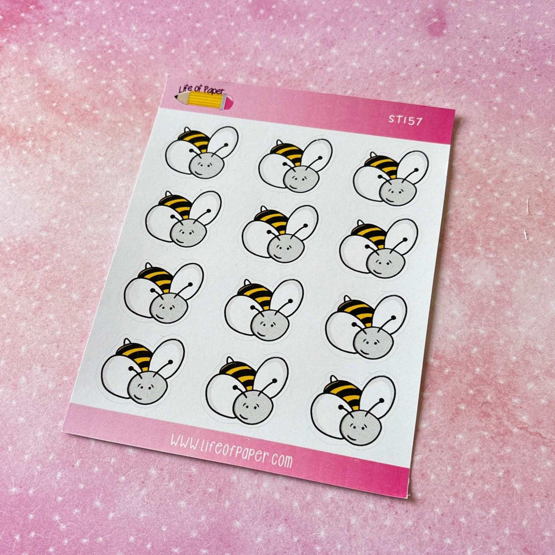 The Bumblebee Sticker Sheet features twelve cartoon bumblebee stickers set against a speckled pink background. Each bee is illustrated with a white head, yellow and black striped body, and delicate wings. These charming stickers are perfect for enhancing your diary or journal!