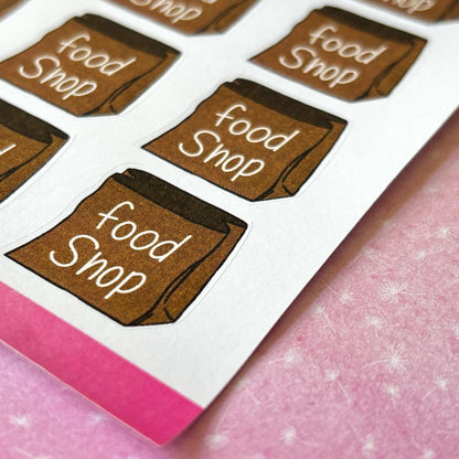 Food Shop Planner Stickers featuring whimsical "food Shop" text on brown paper bag illustrations are perfect for enhancing your planner or journal. Each sheet of these charming stickers is presented against a light pink background.