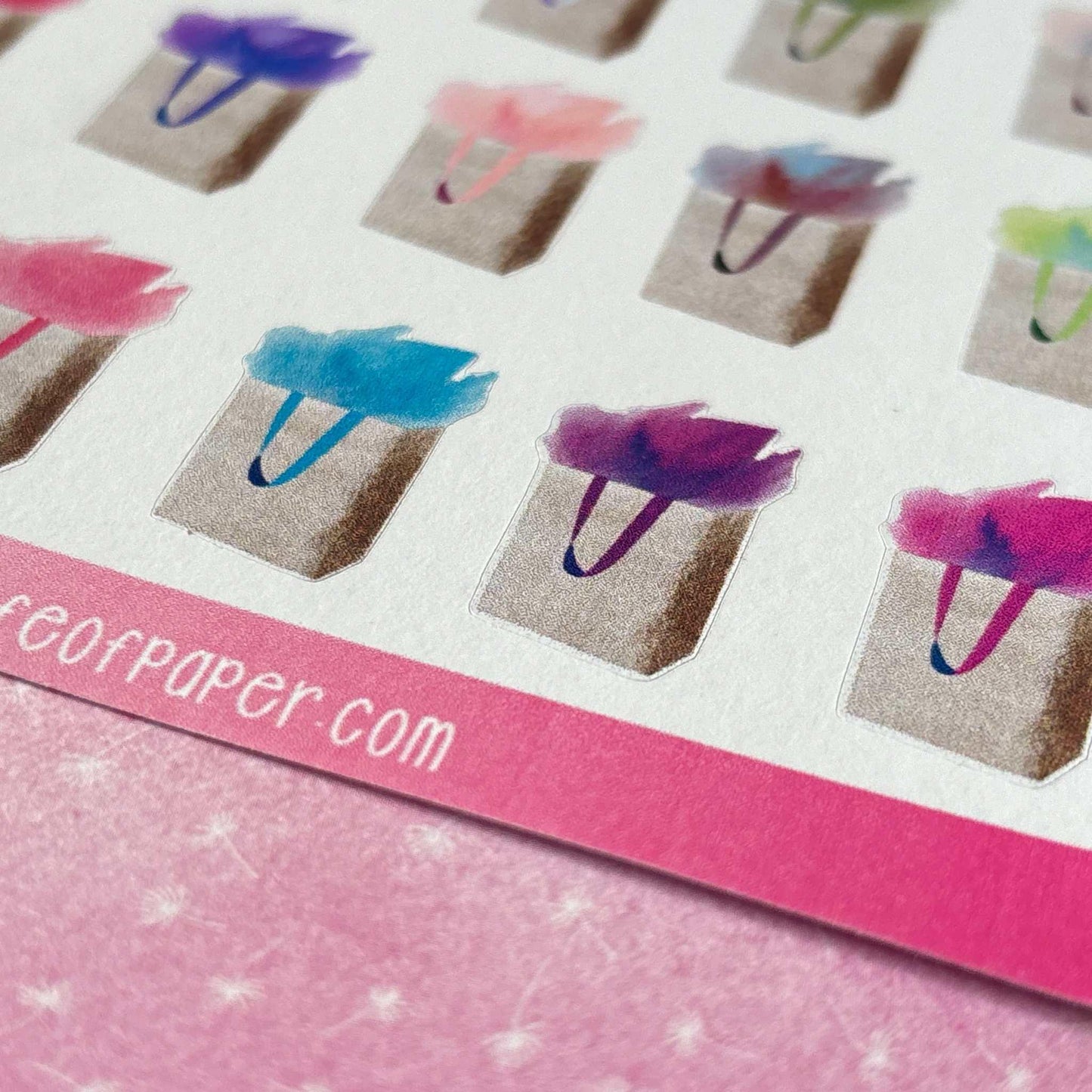 Gift Bag Stickers featuring colorful tissue paper are arranged in rows. A visible pink border at the bottom showcases partial text ending in "paper.com." The background surface is pink with a subtle pattern, making these perfect planner stickers for any gift reminder.