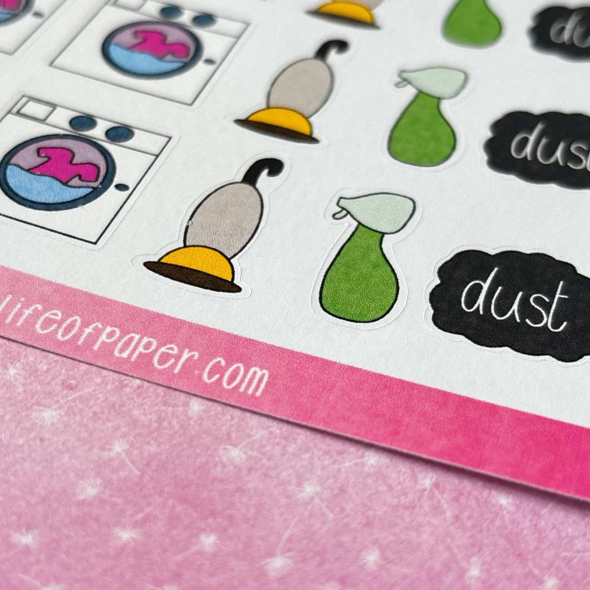 A close-up of a sheet of Cleaning Planner Stickers, showcasing images of a washing machine, vacuum cleaner, spray bottle, and the word "dust" against a pink and white background. Ideal for making your Cleaning Planner both fun and efficient!