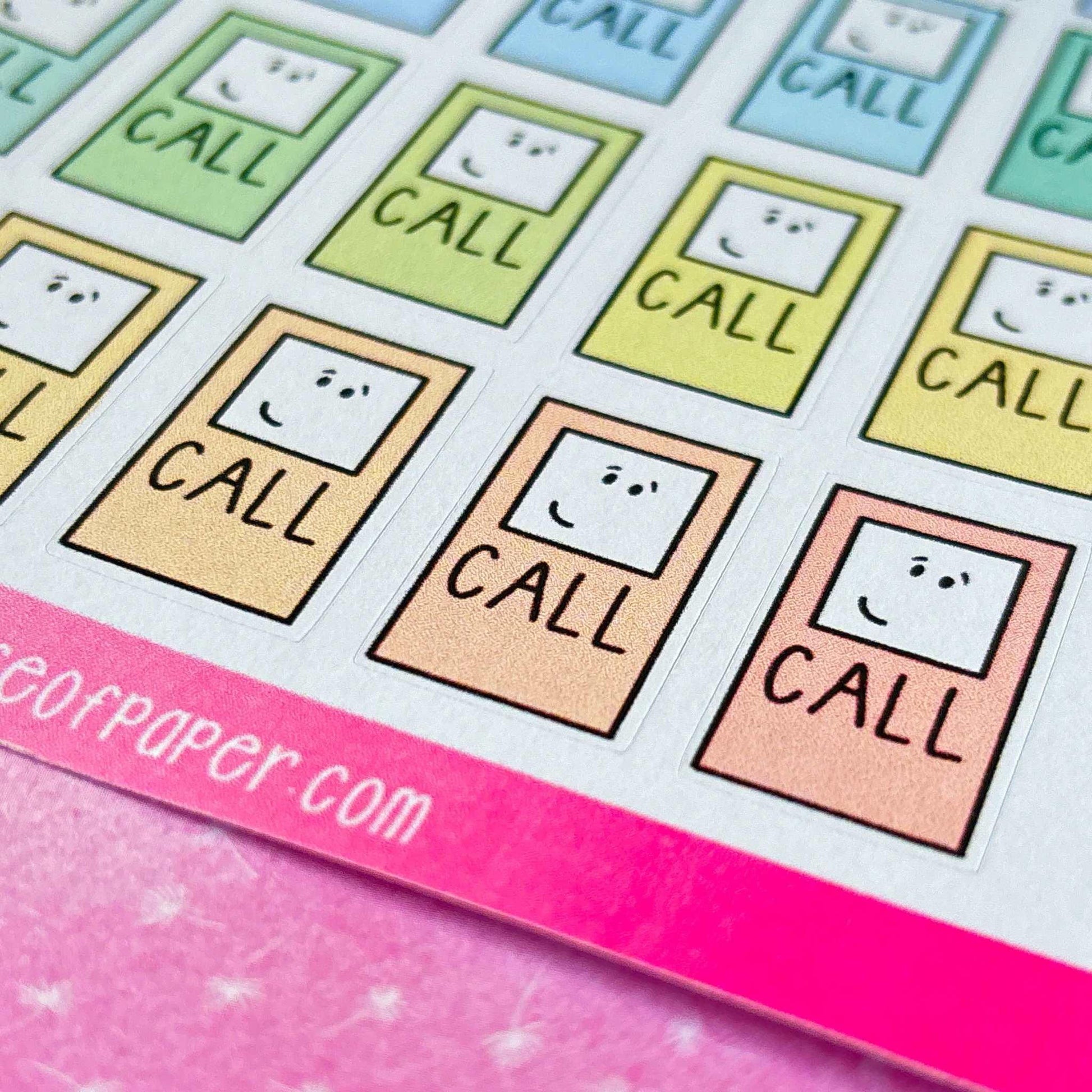 A sheet of Call Reminder Planner Stickers, adorned with each sticker featuring a smiling face and the word "CALL." The stickers are ideal for planner organization and come in vibrant shades of green, yellow, blue, and pink. The sheet is partially shown on a pink surface.