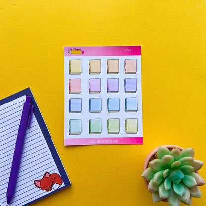 A sheet of Bookworm Stickers, perfect for planner decoration, is placed on a bright yellow surface. Next to it, there's a notepad with a purple pen and a small illustrated fox on the bottom corner. On the right, there's a potted succulent plant.