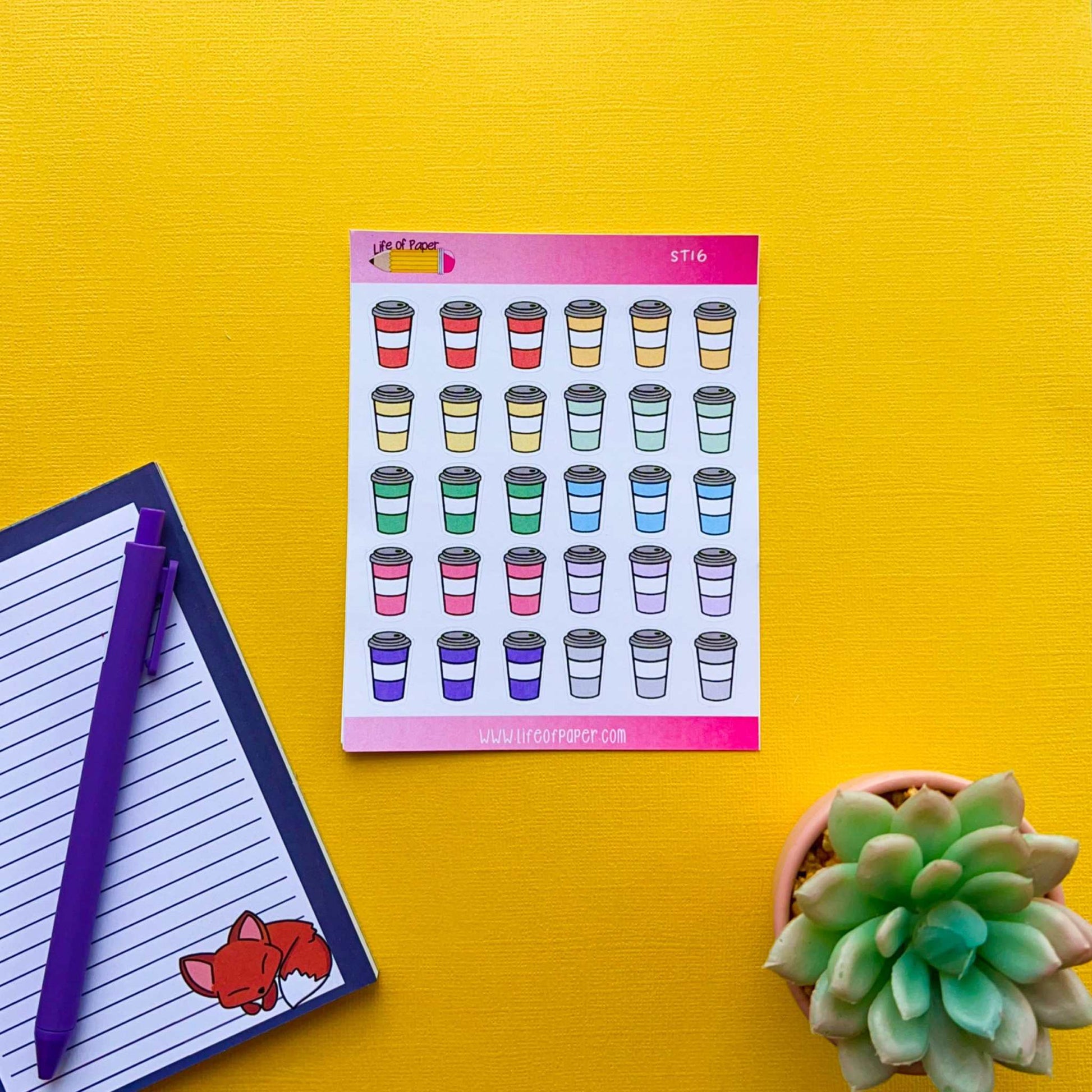 A sheet of Rainbow Coffee Cup Planner Stickers on a yellow background. To the left, a notepad with a fox at the bottom and a purple pen are placed. A small green succulent in a pot is on the right.