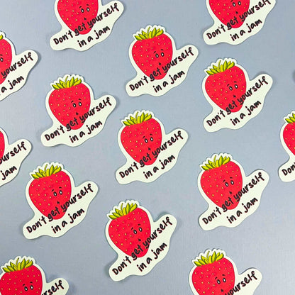 Don't get in a Jam Vinyl sticker featuring illustrated strawberries with cute faces and the text "Don't get yourself in a jam" arranged in a pattern on a light blue background. Perfect as a vinyl strawberry sticker for any surface!
