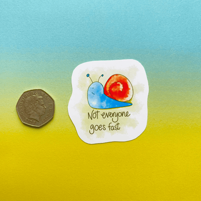 A water-resistant sticker called the Speedy Snail - Animal Vinyl Sticker showcases a cartoon snail with the text "Not everyone goes fast." It features a vibrant gradient background of blue and yellow, with a British five pence coin included for scale.