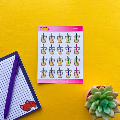 A sheet of Iced Coffee Planner Stickers lies on a bright yellow surface. Next to it are a lined notepad with an orange fox illustration and a purple pen. A green succulent plant in a white pot is also visible in the bottom right corner. This cheerful setup is perfect for summer cold drinks-themed planner stickers!