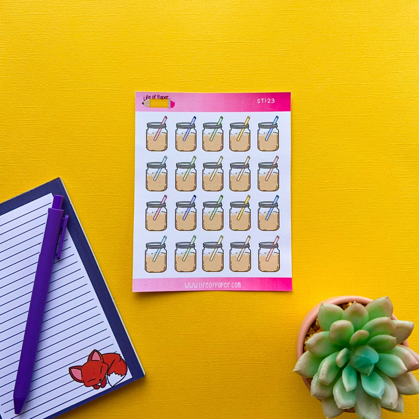 A sheet of Mason Coffee Jar Planner Stickers is displayed on a bright yellow background. To the left, there is a blue notebook with lined paper and a fox illustration, and a purple pen. On the bottom right, there's a green succulent plant.