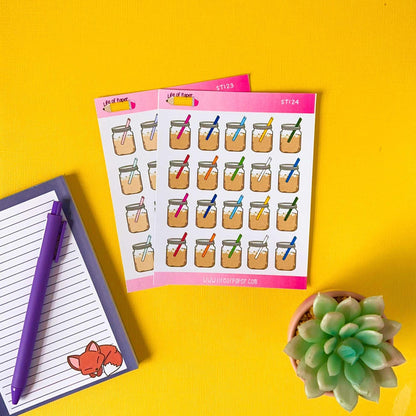 A sheet of Mason Jar Stickers featuring various bow colors, a lined notepad with a pen and a fox illustration in the corner, and a small potted succulent, all arranged on a bright yellow surface.