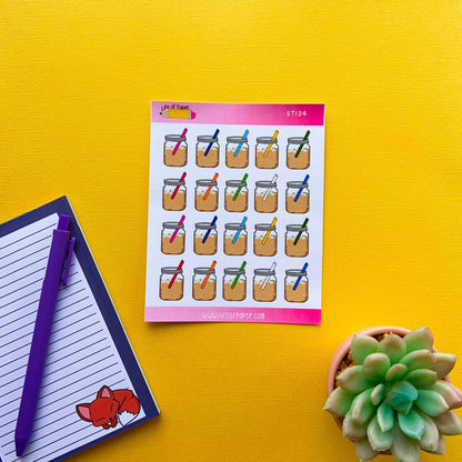 A sheet of Mason Jar Stickers featuring colorful planner stickers with straws and ribbon bows, a notebook with a purple pen, and a small succulent plant are all set against a yellow background.