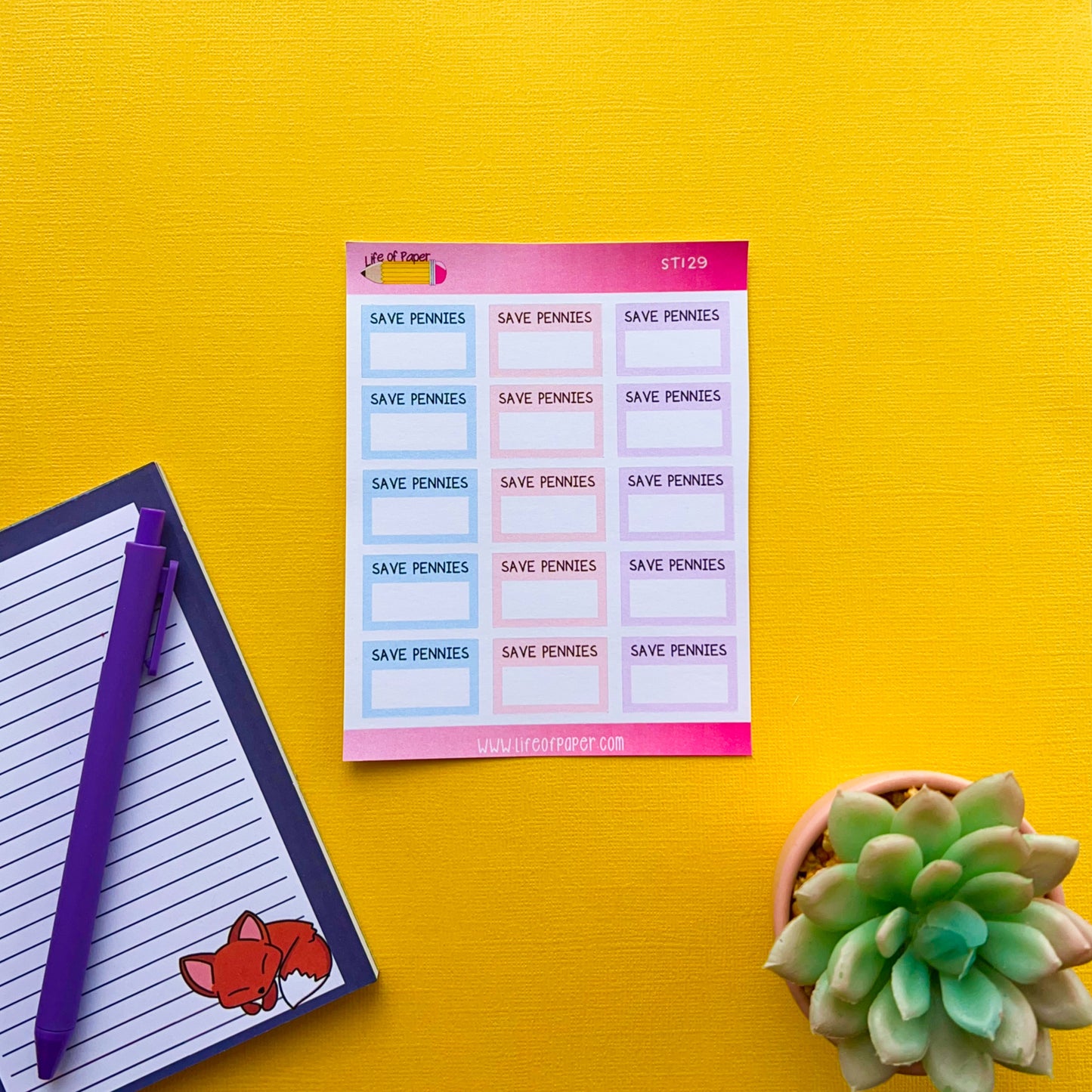 A sheet of colorful "Saving Amount Planner Stickers" is placed on a bright yellow surface. Next to it, there is a small lined notepad with a fox illustration in the corner and a purple pen resting on it. A succulent plant completes this cheerful setup, perfect for any Save Money Planner enthusiast.