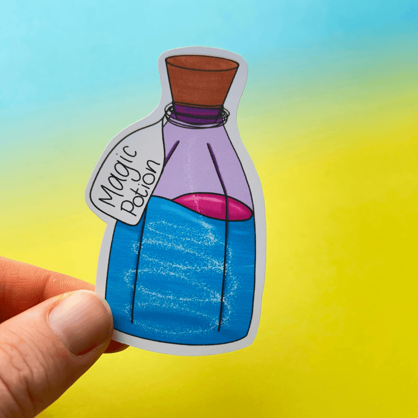 A hand holds the "Magic Potion Sticker," featuring a bottle labeled "Magic Potion" with a cork stopper, partially filled with blue and pink liquid, against a blue and yellow background. The sticker is crafted from strong matte vinyl.