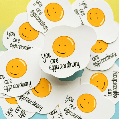 A stack of Extraordinary Silly Pun Quote Vinyl Stickers, featuring a smiling fried egg illustration and the text "You are eggtraordinary," makes for a perfect gift for friends.