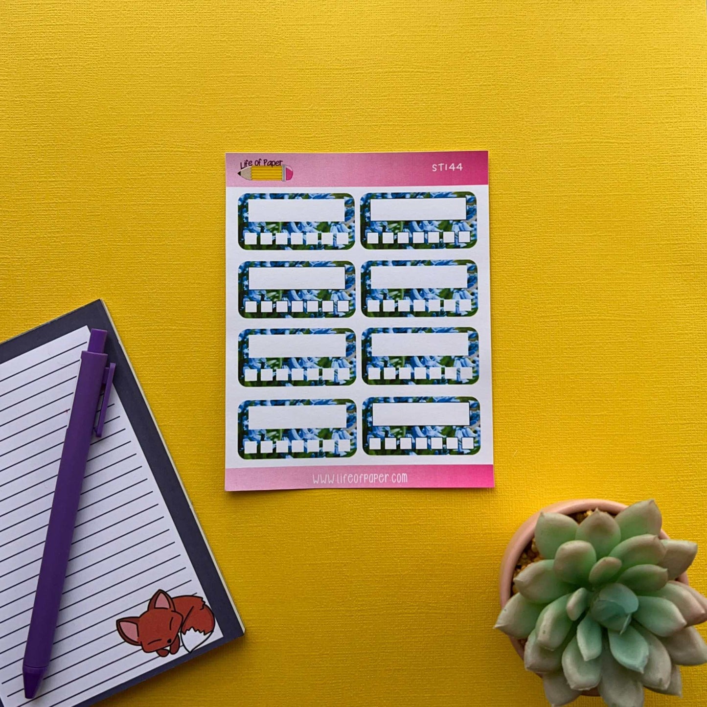A sheet of Weekly Habit Tracker Planner Stickers, ideal as habit tracking stickers, is placed on a yellow surface. Next to it, there is an open notepad with a purple pen on top. A small, potted succulent plant sits nearby.
