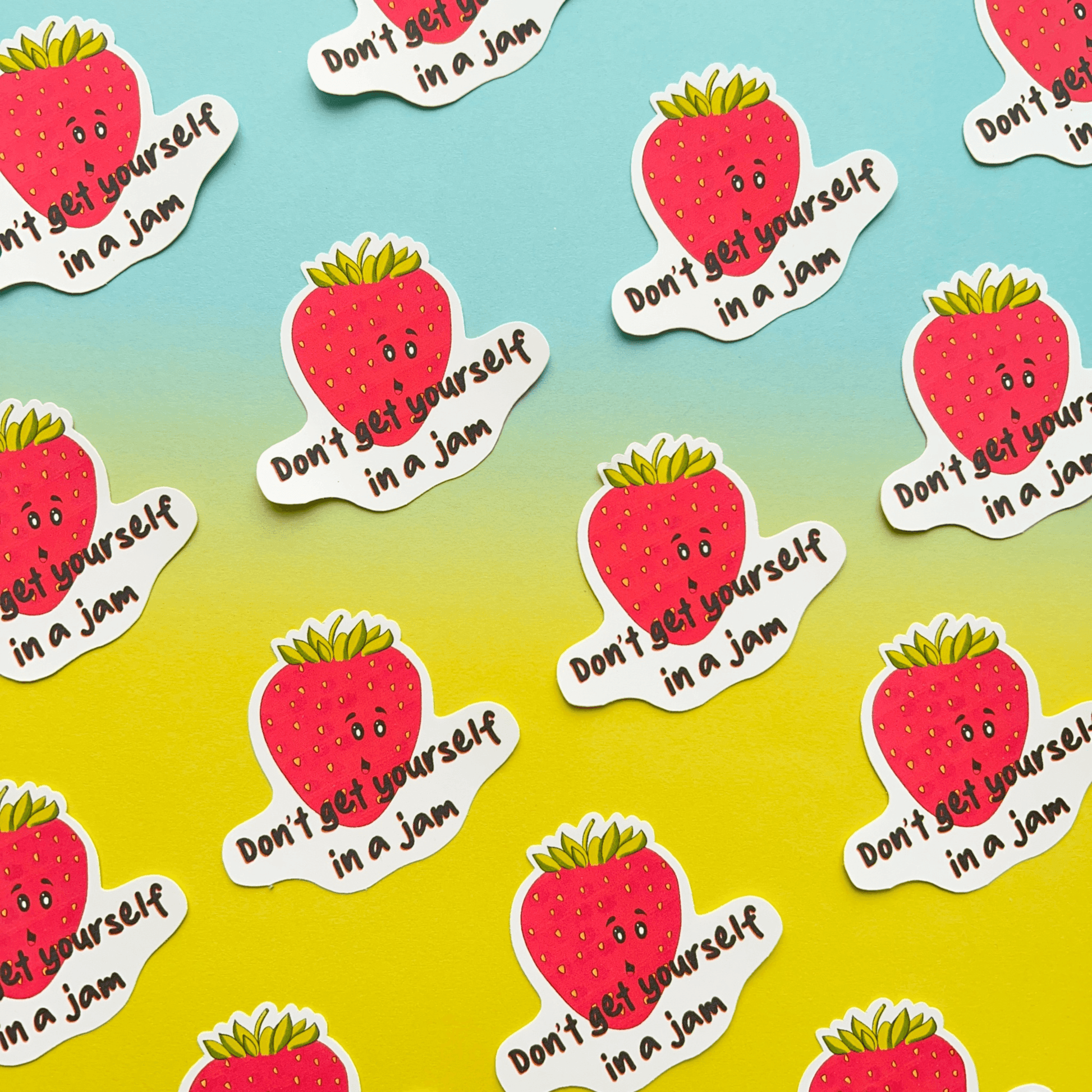 Strawberry Stickers featuring smiling strawberries and the phrase "Don't get yourself in a jam" are arranged in a pattern on a gradient blue-to-yellow background. These water-resistant vinyl stickers are perfect for adding a touch of humor with their jammy pun.