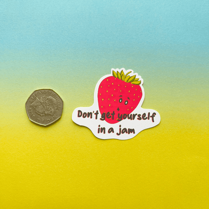 The Strawberry Sticker features a water-resistant vinyl design with a cartoon strawberry that has a face and the text "Don't get yourself in a jam." It is shown next to a coin for size comparison, placed on a gradient yellow to blue background.