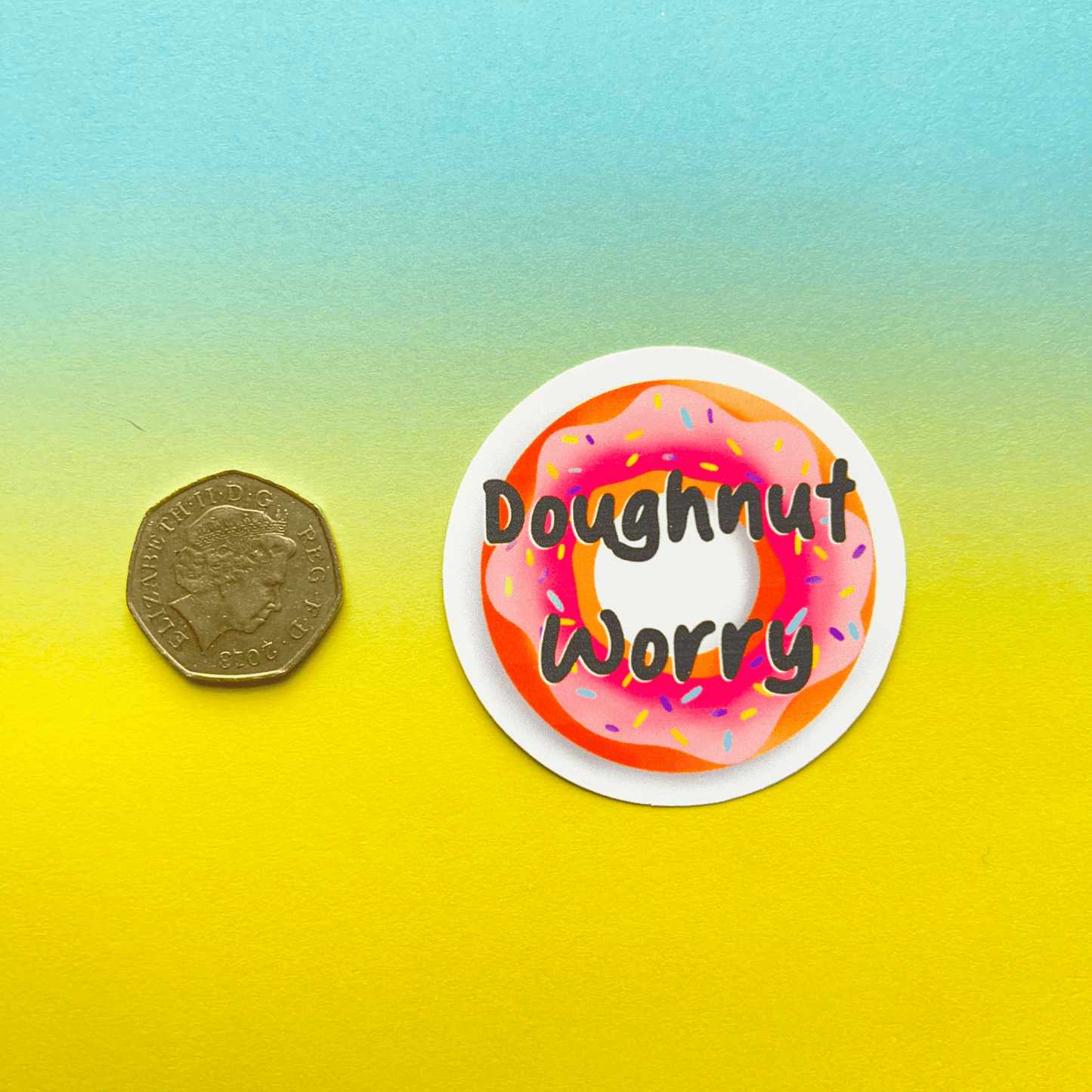 A coin is placed next to the Doughnut Sticker, a strong matte vinyl sticker featuring a pink frosted doughnut with sprinkles and the text "Doughnut Worry" on a pastel background.