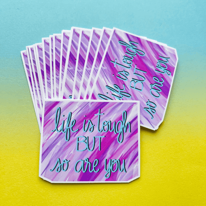 Introducing the 'Life Is Tough Affirmation Vinyl Sticker' with a colorful background and motivational text saying, 'Life is tough BUT so are you,' printed on strong matte vinyl.