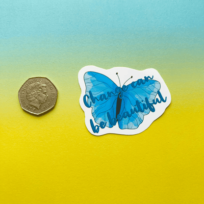 An illustration of the "Change can be Beautiful Vinyl Sticker," depicting a blue butterfly with the text “Change can be beautiful” next to a 50-pence coin, is displayed on a background with a gradient transitioning from blue to yellow. This sticker is perfect for creating motivational displays or matte vinyl applications.