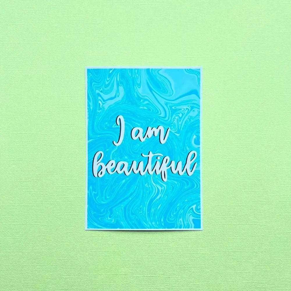 An Affirmation Postcard featuring a textured green background and a blue marble design at the center, showcasing the phrase "I am beautiful" in elegant white cursive lettering. Ideal for admirers of inspirational quotes.