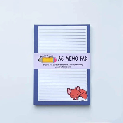 A blue A6 Animal Collection Memo Pads with lined paper, featuring a cute illustration of an orange fox in the bottom right corner. The pad has a label with a pencil graphic that reads "A6 MEMO PAD" and the website "www.lifeofpaper.com". Perfect for those who love animal memo pads or as part of a charming gift set.