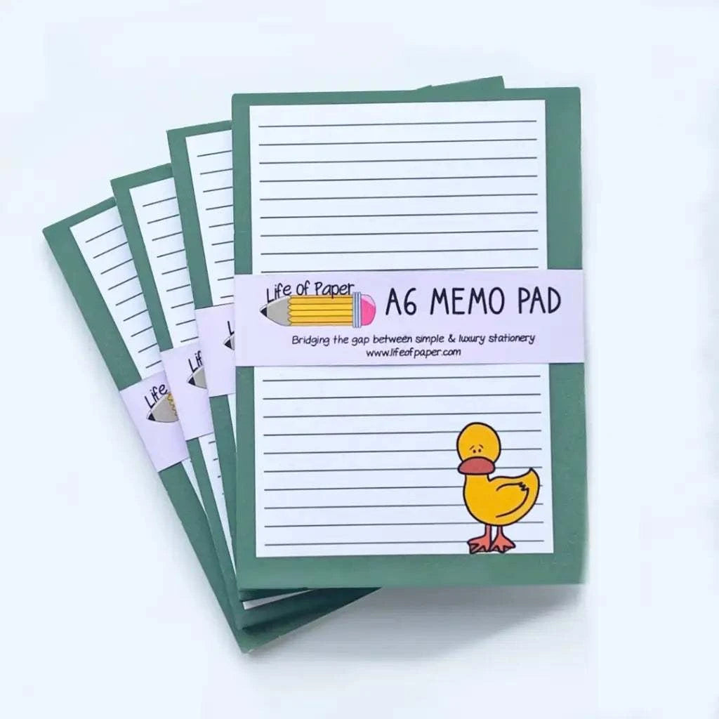 A stack of A6 memo pads is shown with green covers and a lined paper design. Each mini memo pad features a small duck illustration at the bottom right corner and is fountain pen friendly. A label wrapped around the pad reads, "Duck Memo Pad" with a pink pencil icon.