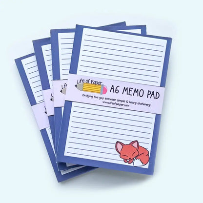 Four A6-sized Fox Memo Pads are stacked, featuring a blue border and lined pages. The cover shows a cute sleeping fox illustration in the bottom right corner. Branded "Life of Paper," these memo pads are fountain pen friendly, with a tagline and website link included.