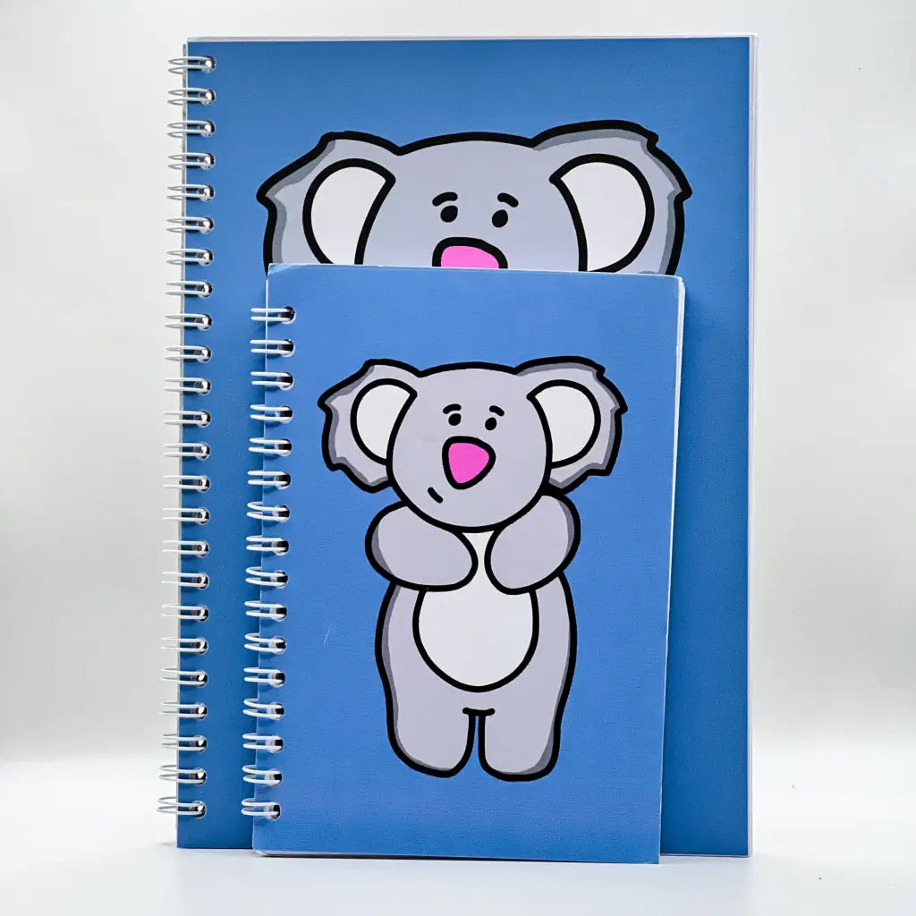 Two spiral-bound Gentle Koala Notebooks with blue covers are displayed. Each cover features a cartoon koala illustration. The larger notebook, ideal for note-taking, has a head-on view of the koala's face, while the smaller, 40-page notebook displays the entire body of the koala. The background is plain white.