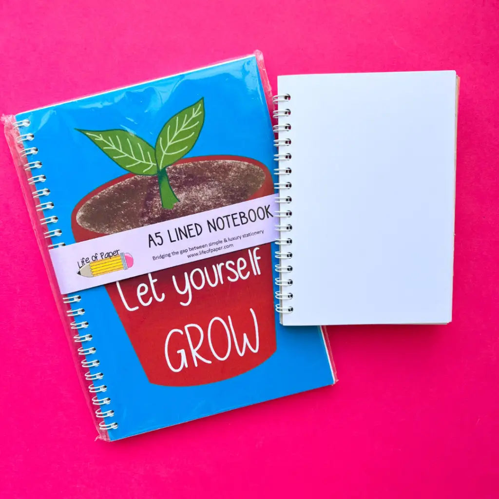 A Let Yourself Grow Notebook with a cover illustration of a plant pot and the positive quote "Let yourself GROW" lies on a vivid pink background. Beside it is another smaller spiral-bound white notebook with a blank cover. Both notebooks have white spirals, perfect for boosting self-esteem.