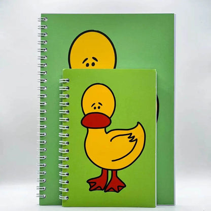 Two spiral-bound Mini Worried Duck Notebooks with green covers, featuring a yellow duck with a red beak and feet. One notebook is larger and partially covers the smaller one, showing a full duck on the small notebook (40 pages) and only the duck's head on the large one.