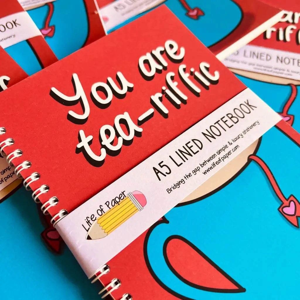 Close-up of a red spiral-bound notebook with "You are tea-riffic" on the cover. This A6 plain notebook features 40 pages, perfect for note-taking, and showcases a logo with a pencil and the text "Life of Paper.