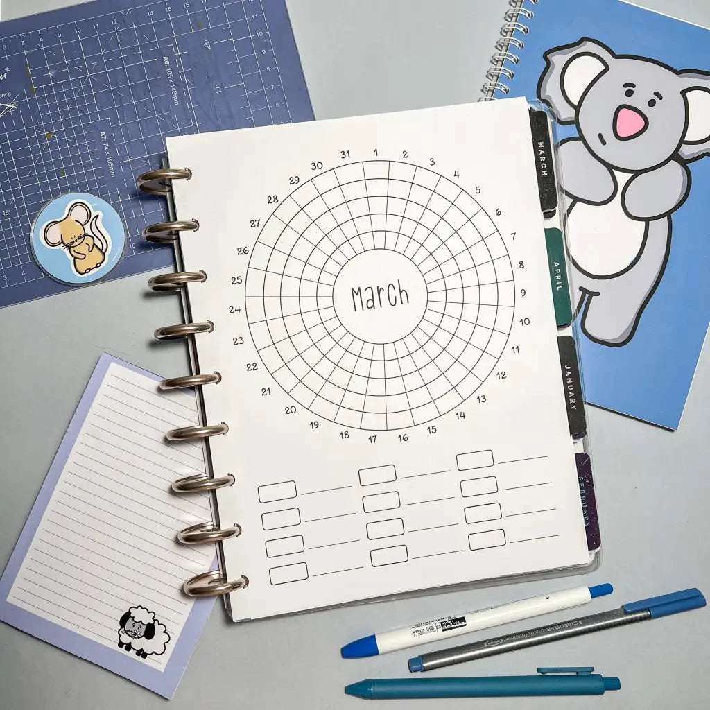 A Monthly Habit Tracker for March is open in the center of the image, surrounded by stationery items including a blue notebook with a koala illustration, a blue grid ruler, a memo pad with a sheep, and three pens. The background is a light gray surface perfect for incorporating your monthly habit tracker or goal setting notes.