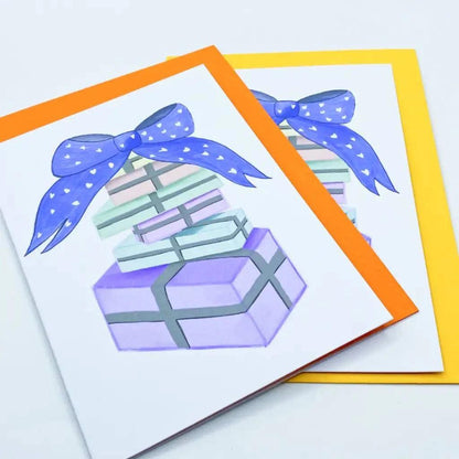 The Pastel Birthday Card set includes two delightful designs featuring an illustration of stacked pastel-colored birthday gifts tied with a blue ribbon. Perfect for any celebration, one card boasts an orange border while the other showcases a cheerful yellow border.