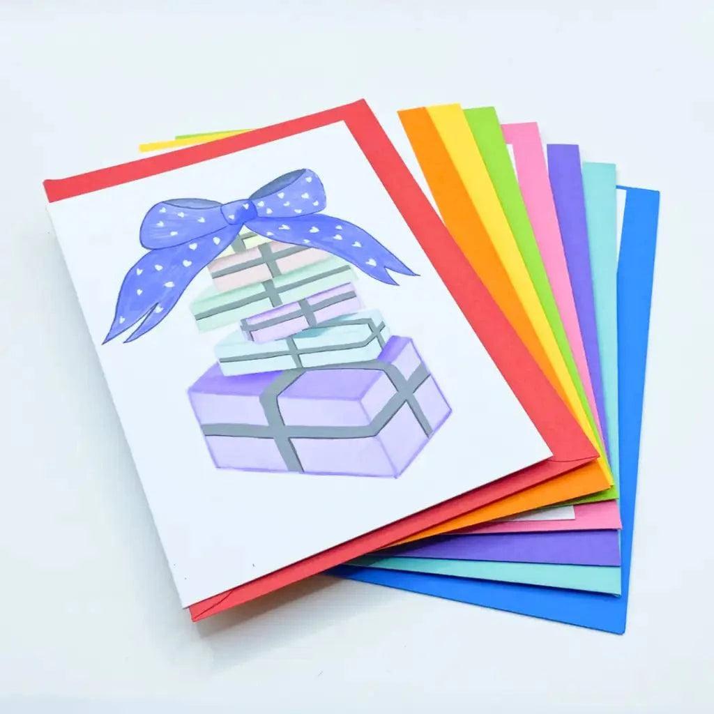 A stack of Pastel Birthday Cards with the top card featuring an illustration of three birthday gifts stacked on top of each other, tied with a purple bow.