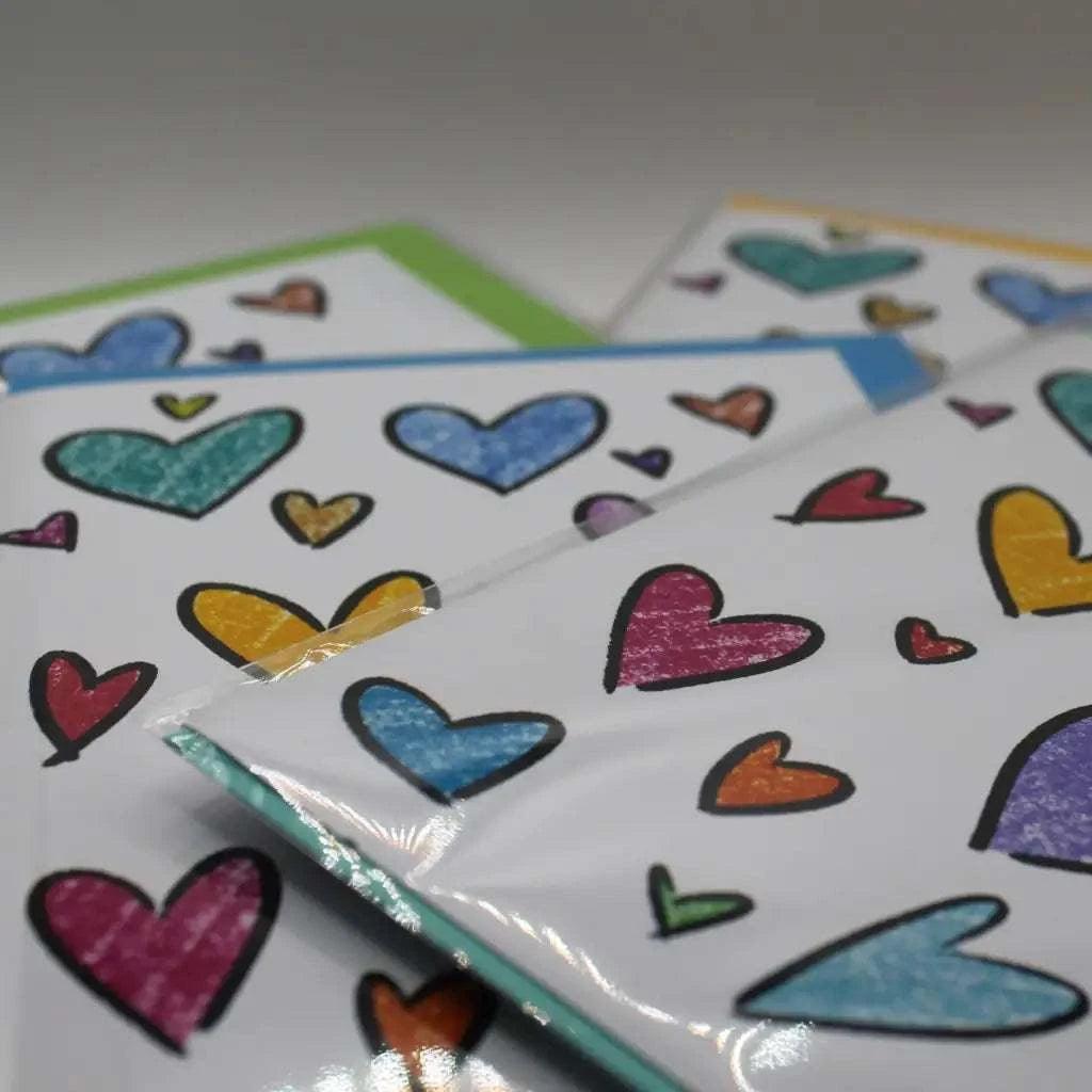 Introducing the Rainbow Hearts Greeting Card: a collection of biodegradable greeting cards adorned with vibrant, hand-drawn hearts in various sizes, elegantly displayed on a clear surface.