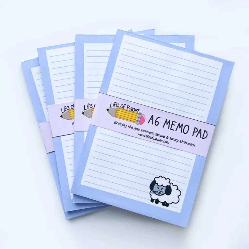 The image shows four stacked A6, handmade memo pads with light blue covers. A paper band labeled "Sheep Memo Pad" wraps each pad, featuring a pencil and a sheep illustration. These mini memo pads have lined, fountain pen friendly pages, and the brand slogan and website are also displayed.