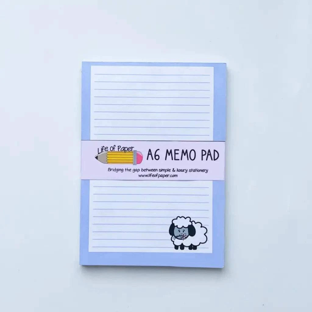 A vertical A6 memo pad with a light blue cover and a wraparound band. The band reads: "Sheep Memo Pad - Bridging the gap between simple & luxury stationery www.lifeofpaper.com". This handmade memo pad features a pencil icon, a small drawing of a sheep, and is fountain pen friendly.