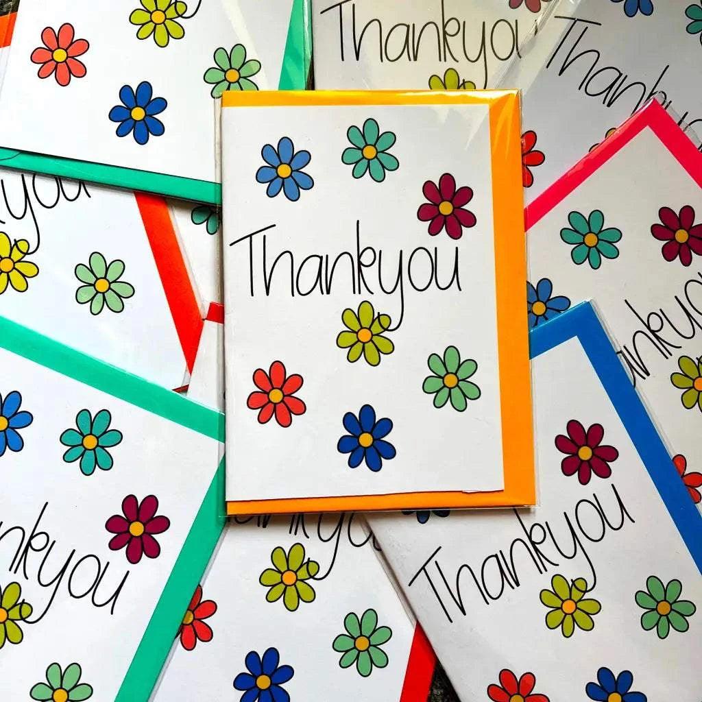 The Thank You Card collection offers colorful and vibrant thank-you cards adorned with beautiful flower illustrations. Each card features "Thank you" written in elegant black cursive on the front and comes enclosed in a biodegradable cellophane bag. The designs are enhanced by different colored borders, creating a cheerful arrangement with blank spaces inside for personalized messages.