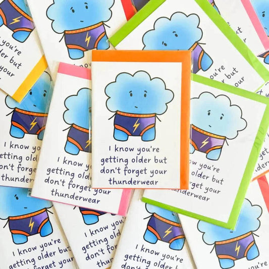 The Thunderwear Blank Birthday Card showcases a whimsical illustration of a cute, blue cloud character dressed as a superhero, complete with a lightning bolt on its chest. Each humorous birthday card bears the message, "I know you're getting older but don't forget your thunderwear," and is packaged in biodegradable materials.